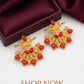 Gold earrings with red stones on a white surface with a maroon box in the background.