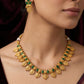 Gold necklace with green stones worn by a model against a dark background