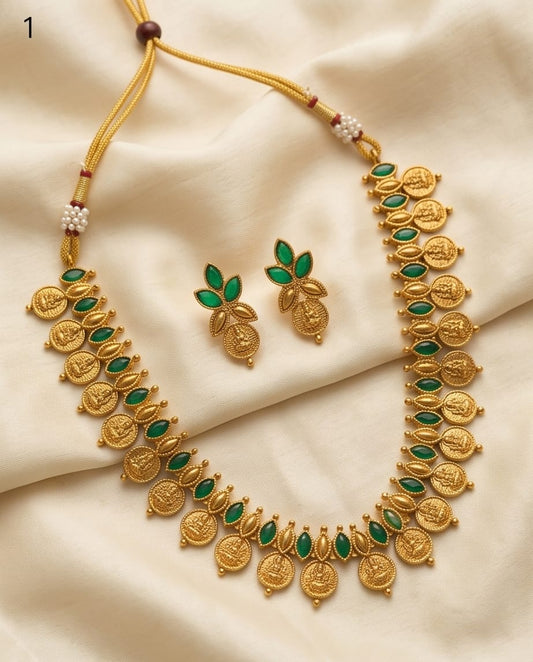 Gold necklace with green stones and matching earrings on a beige fabric background