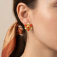 Close-up of a woman wearing gold earrings with red and white stones against a neutral background