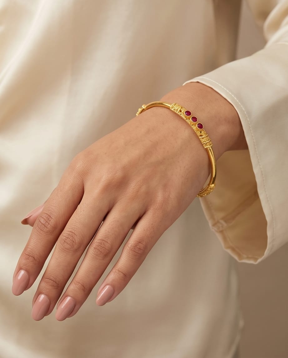 Gold bracelet with red stones on a hand against a beige background