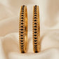 Gold hoop earrings with black beads on a beige fabric background