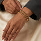 Close-up of a hand wearing a gold bracelet on a neutral background