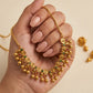 Gold necklace and earrings with gemstones held in a hand against a beige background