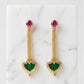 Gold earrings with green and red gemstones on a marble surface