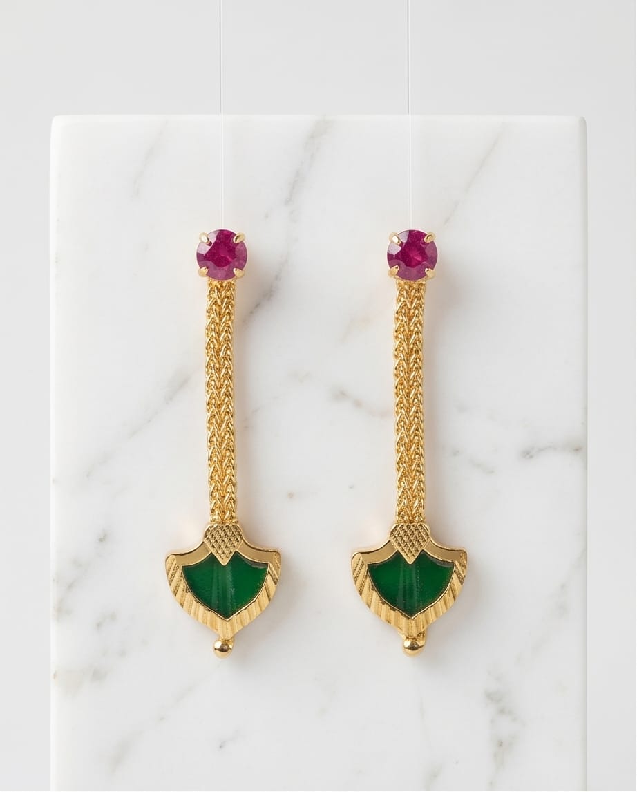 Gold earrings with green and red gemstones on a marble surface