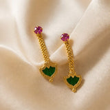 Gold earrings with green and pink gemstones on a beige fabric background