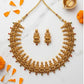Gold necklace and earrings on a marble surface with orange flowers.