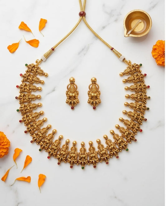 Gold necklace and earrings on a marble surface with orange flowers.