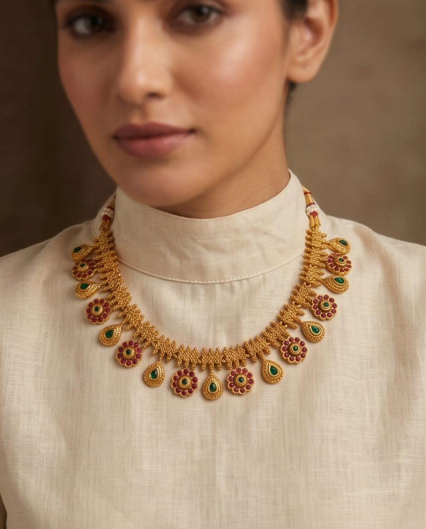 Woman wearing a gold necklace with floral designs on a beige background