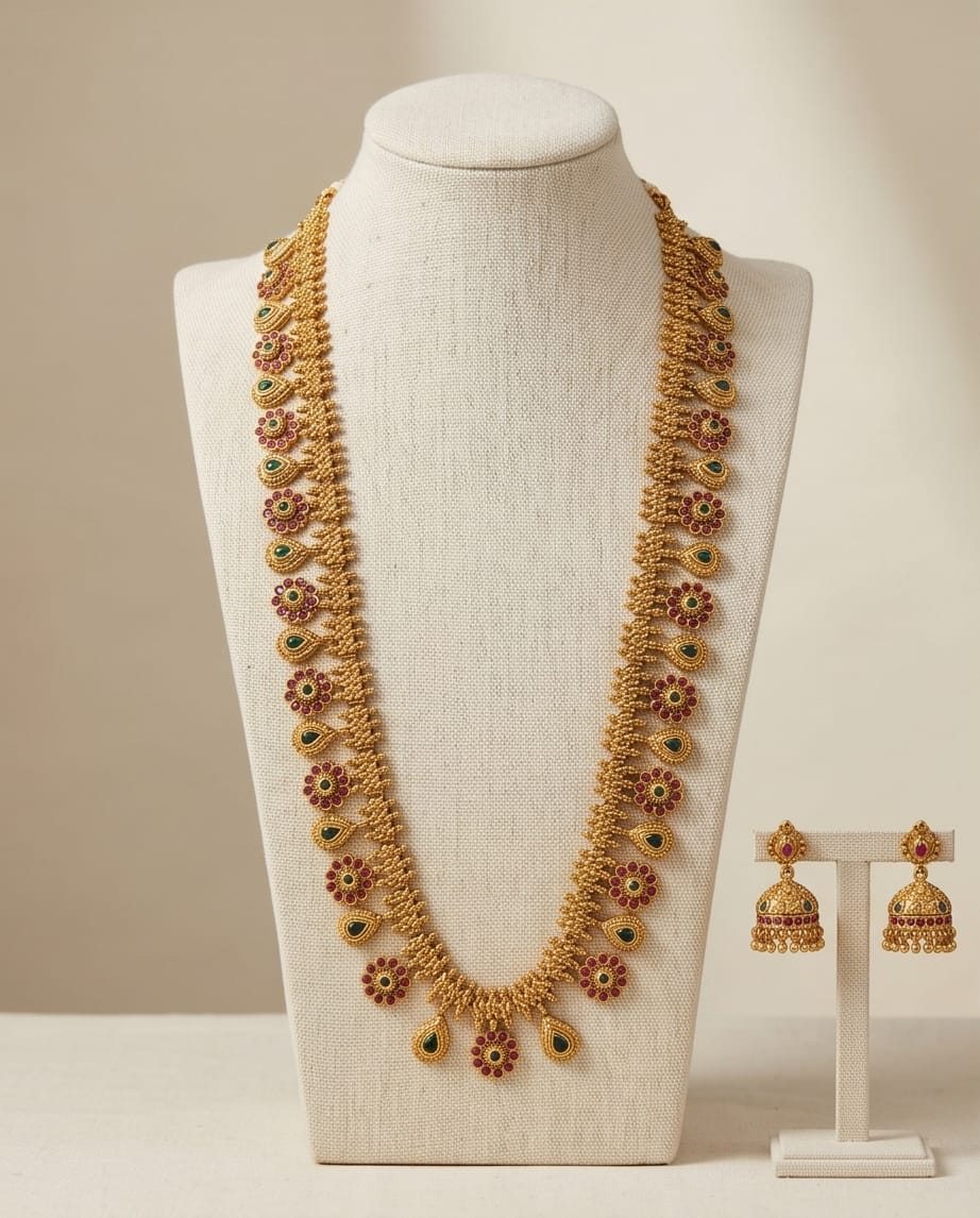 Gold necklace with floral designs on a mannequin bust, accompanied by gold earrings on a stand.