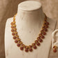 Gold necklace with red stones on a marble mannequin against a beige background