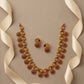 Gold necklace with red stones and matching earrings on a beige background with ribbons.